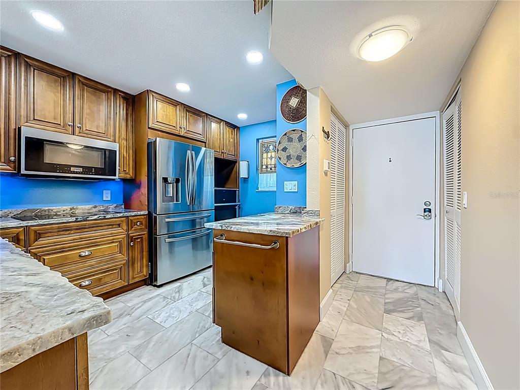 A kitchen features wood cabinetry, stainless steel appliances, granite countertops, and light-colored tile flooring — 18304 GULF BOULEVARD UNIT 505, REDINGTON SHORES, FL