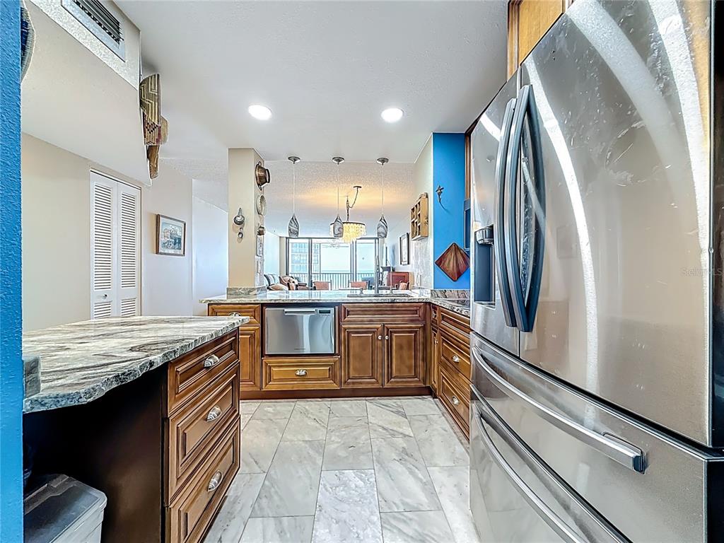 A kitchen features wood cabinets, stone countertops, stainless steel appliances, and light-colored tile flooring — 18304 GULF BOULEVARD UNIT 505, REDINGTON SHORES, FL