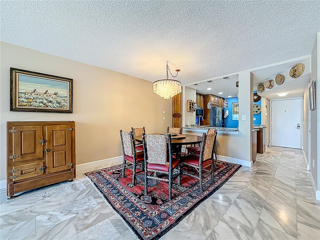 A dining room with a crystal chandelier, patterned rug, marble floors, and adjacent kitchen — 18304 GULF BOULEVARD UNIT 505, REDINGTON SHORES, FL
