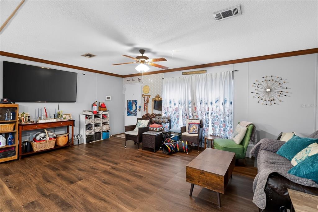 A living room features wood-look flooring, a ceiling fan, a large television, and floral curtains — 5576 S SHALIMAR POINT, HOMOSASSA, FL