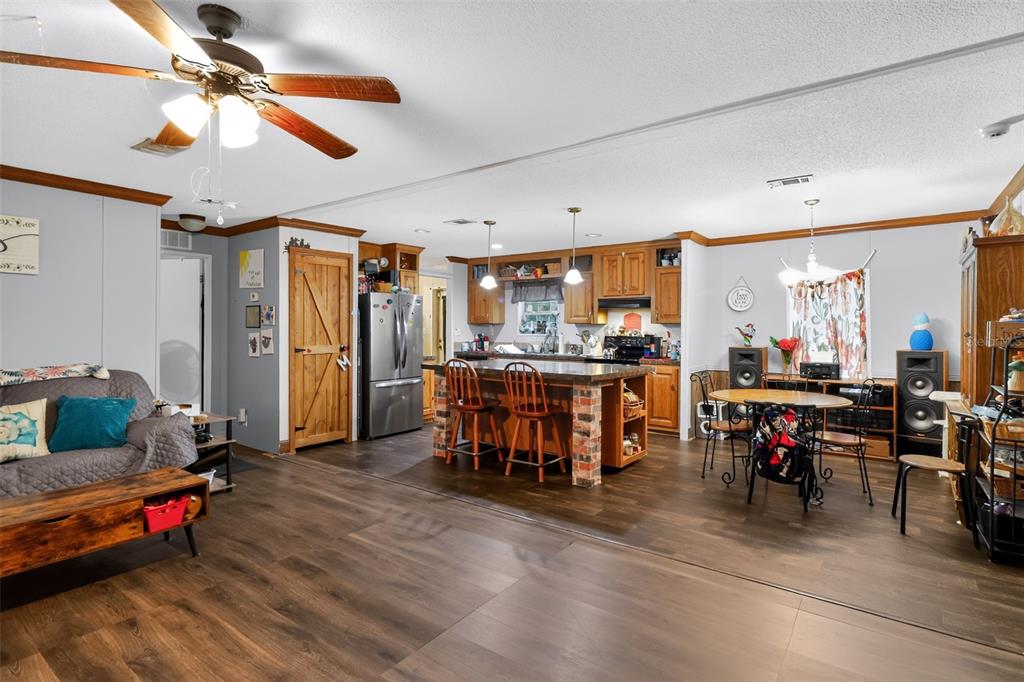 An open-concept kitchen and living area features wood-look flooring, a brick-base island, and wooden cabinetry — 5576 S SHALIMAR POINT, HOMOSASSA, FL