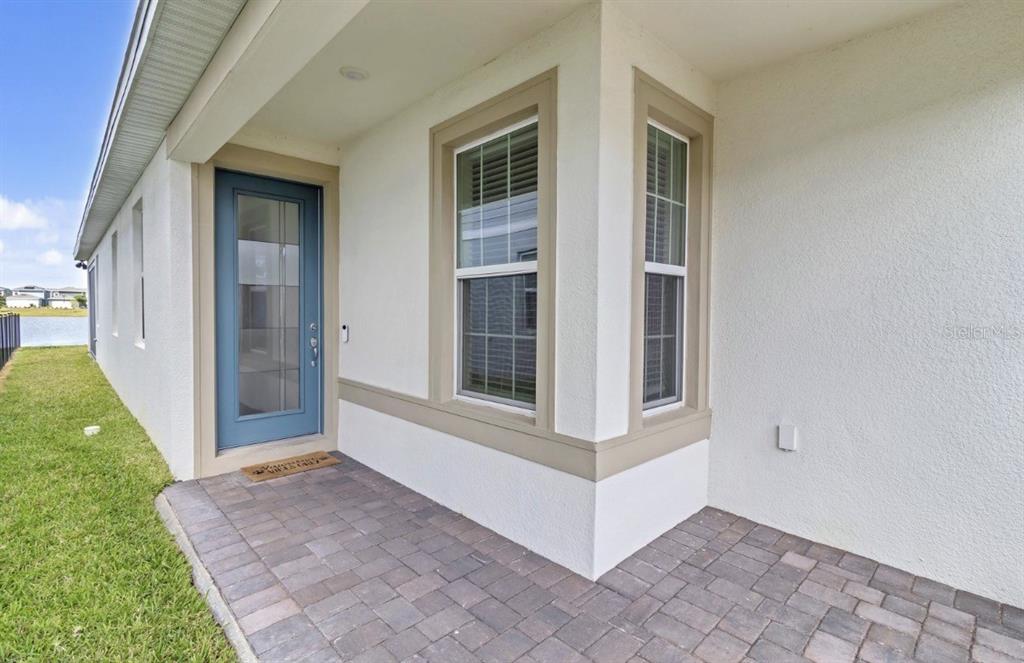 A paved patio area features a blue glass-paneled door and two windows on a stucco wall — 1872 SUMMER SERENITY DRIVE, KISSIMMEE, FL