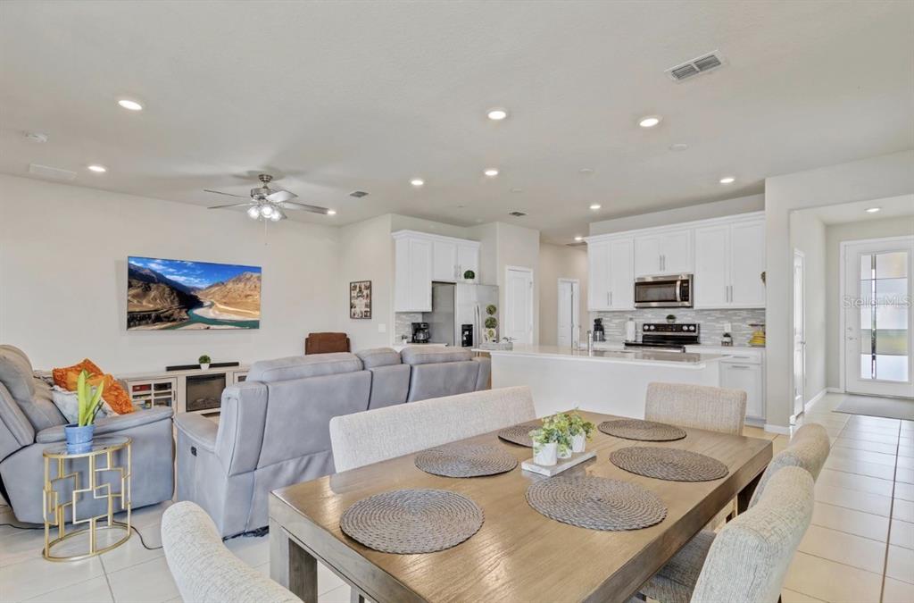 An open-concept living room and kitchen featuring white cabinetry, a dining table, and gray furniture — 1872 SUMMER SERENITY DRIVE, KISSIMMEE, FL