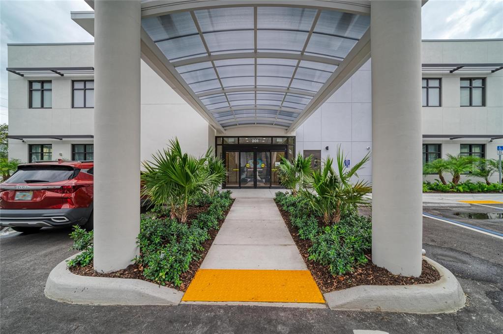 A covered walkway leads to the entrance of a modern commercial building with palm landscaping — 201 5TH AVENUE DRIVE E, BRADENTON, FL