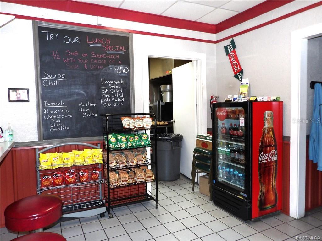 A small restaurant interior features a chalkboard menu, snack racks, and a Coca-Cola refrigerator — 3360 E GULF TO LAKE HIGHWAY, INVERNESS, FL