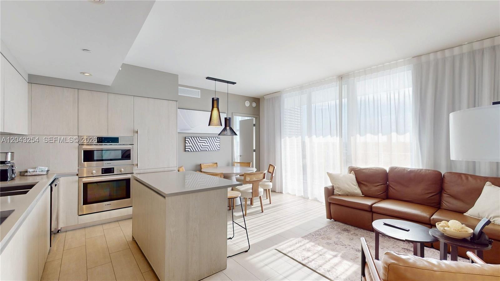 A modern open-concept kitchen and living area features light wood cabinetry and a leather sofa — 4010 S Ocean Dr # R1004, Hollywood FL 33019, HOLLYWOOD, FL
