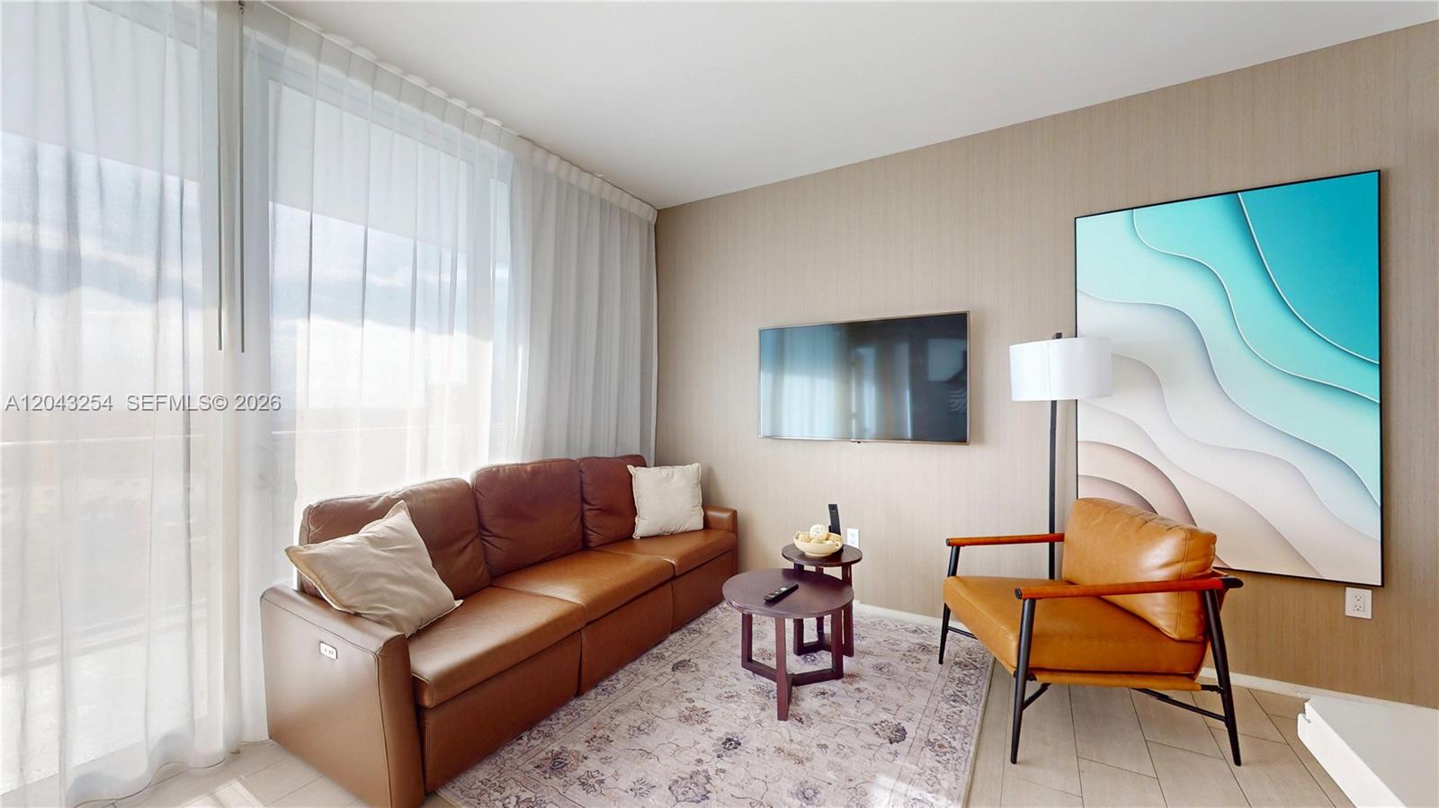 A living room features a brown leather sofa, a matching armchair, and wall-mounted television — 4010 S Ocean Dr # R1004, Hollywood FL 33019, HOLLYWOOD, FL