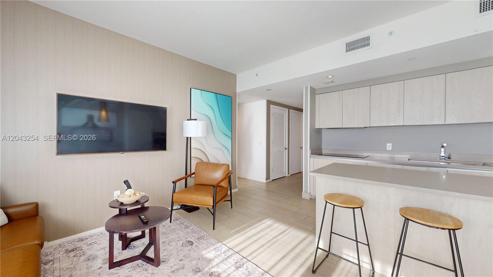 A living room with a wall-mounted television, leather seating, and an adjacent kitchen area — 4010 S Ocean Dr # R1004, Hollywood FL 33019, HOLLYWOOD, FL