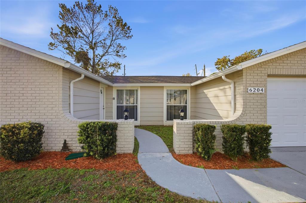 A single-story house exterior features a brick facade, a concrete walkway, and a garage — 6204 WESTPORT DRIVE, PORT RICHEY, FL