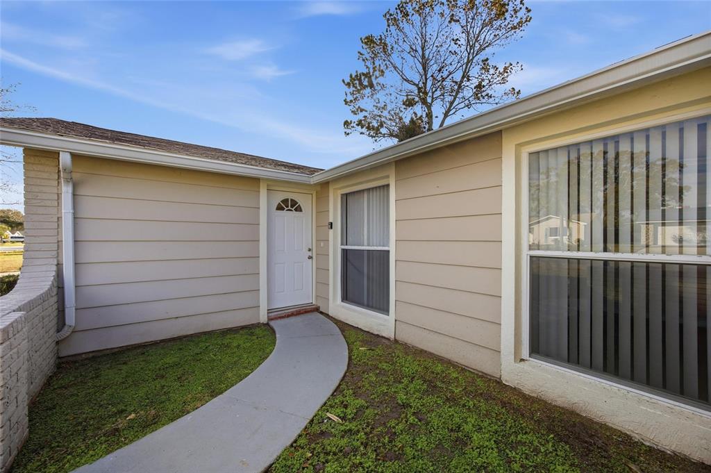 A beige house exterior features a white front door, a concrete walkway, and large windows — 6204 WESTPORT DRIVE, PORT RICHEY, FL
