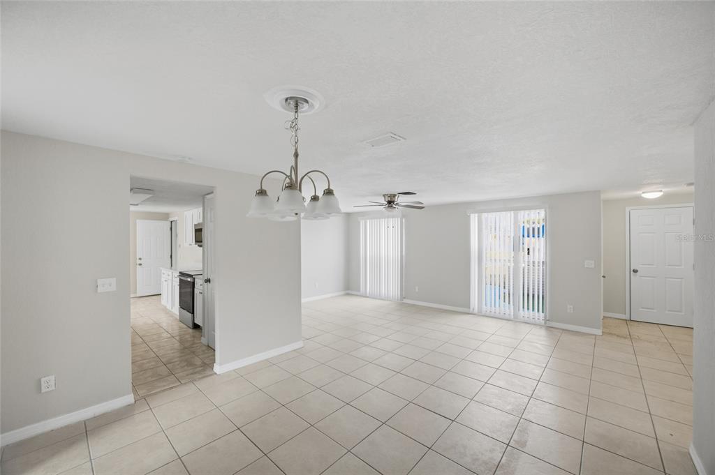 An open-concept living and dining area features light-colored tile flooring and a central chandelier — 6204 WESTPORT DRIVE, PORT RICHEY, FL