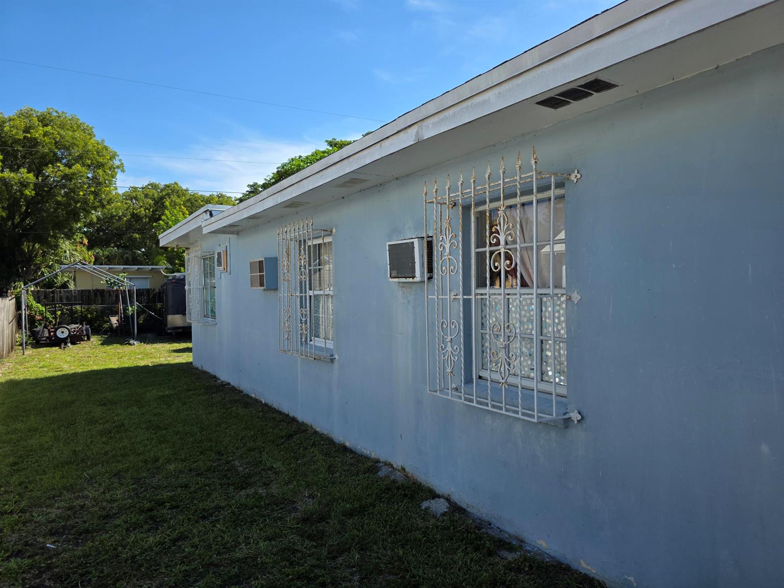 The exterior of a light blue house features white window security bars and an air conditioner — 528 49th Street, West Palm Beach FL 33407, WEST PALM BEACH, FL