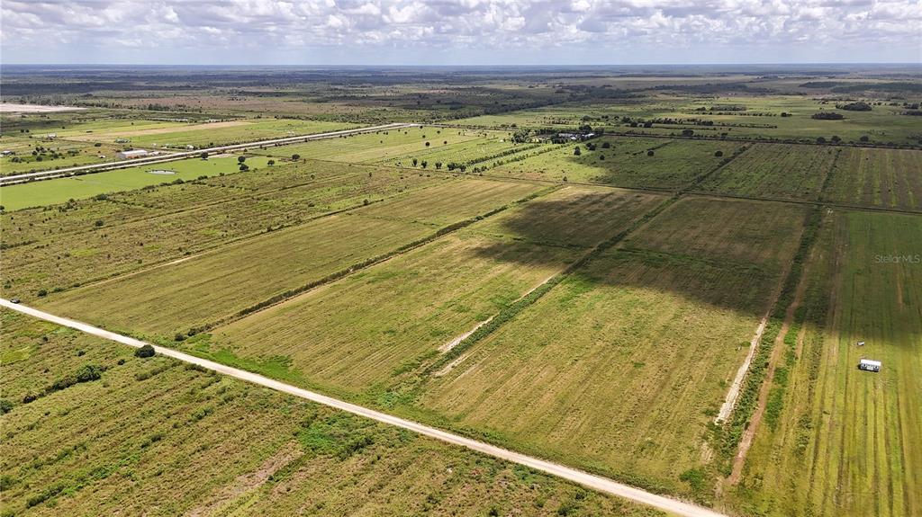 An aerial view shows a large, flat, grassy field bordered by a dirt road — 5595 1ST ROAD, LABELLE, FL