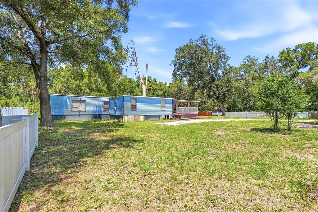 A blue mobile home sits on a large grassy lot surrounded by mature trees — 911 MARJORIE AVENUE, BRANDON, FL