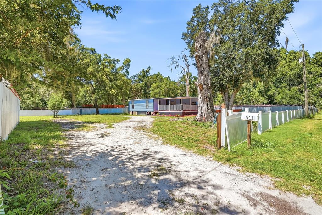 A blue mobile home with a screened porch sits at the end of a dirt driveway — 911 MARJORIE AVENUE, BRANDON, FL