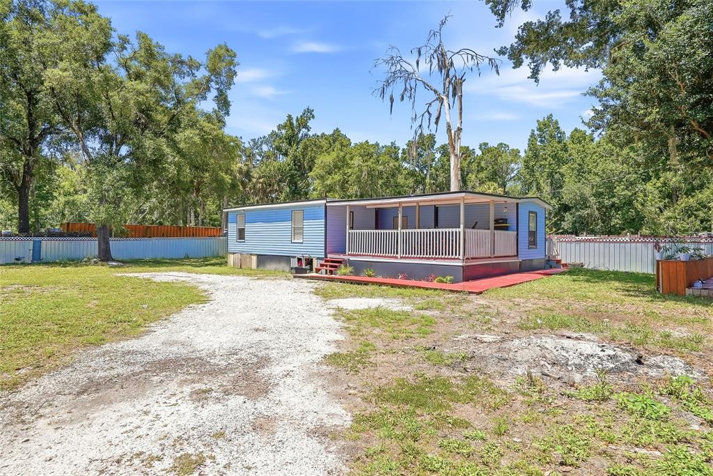 A blue mobile home with a large front porch sits on a gravel driveway — 911 MARJORIE AVENUE, BRANDON, FL