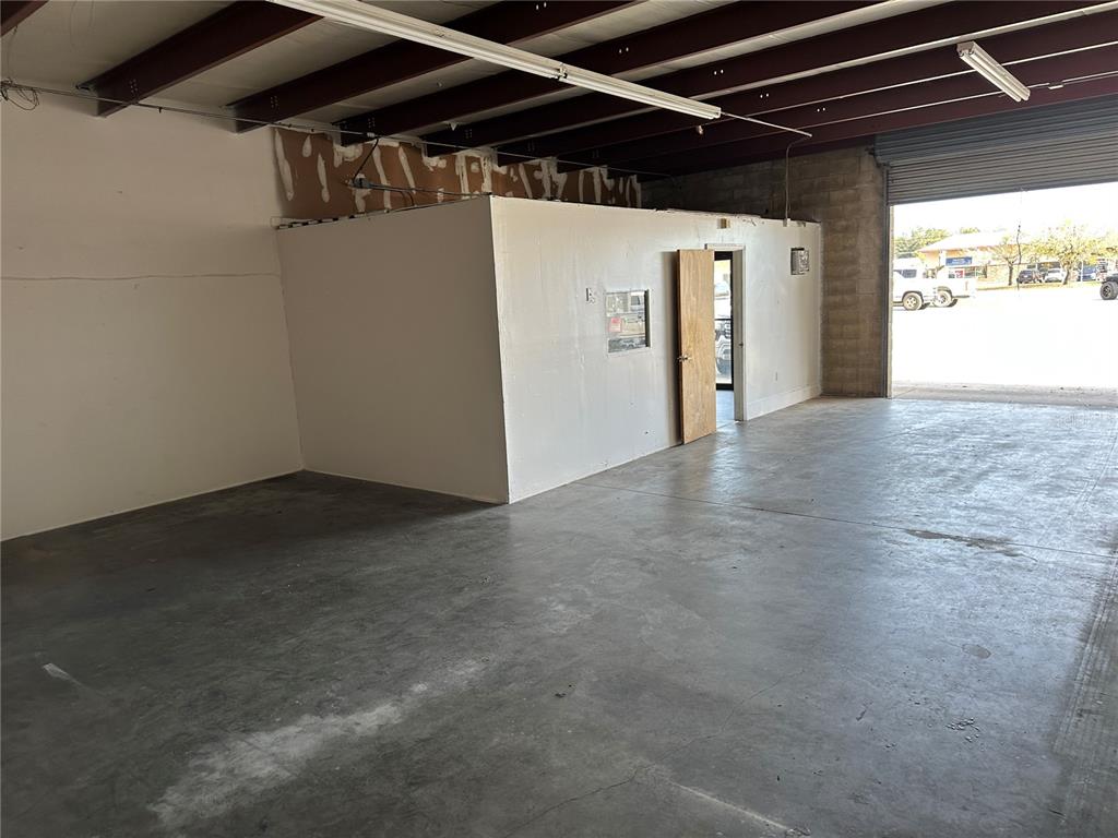 An interior view of a warehouse space featuring a small office enclosure and concrete flooring — 1706 N MAGNOLIA AVENUE, OCALA, FL