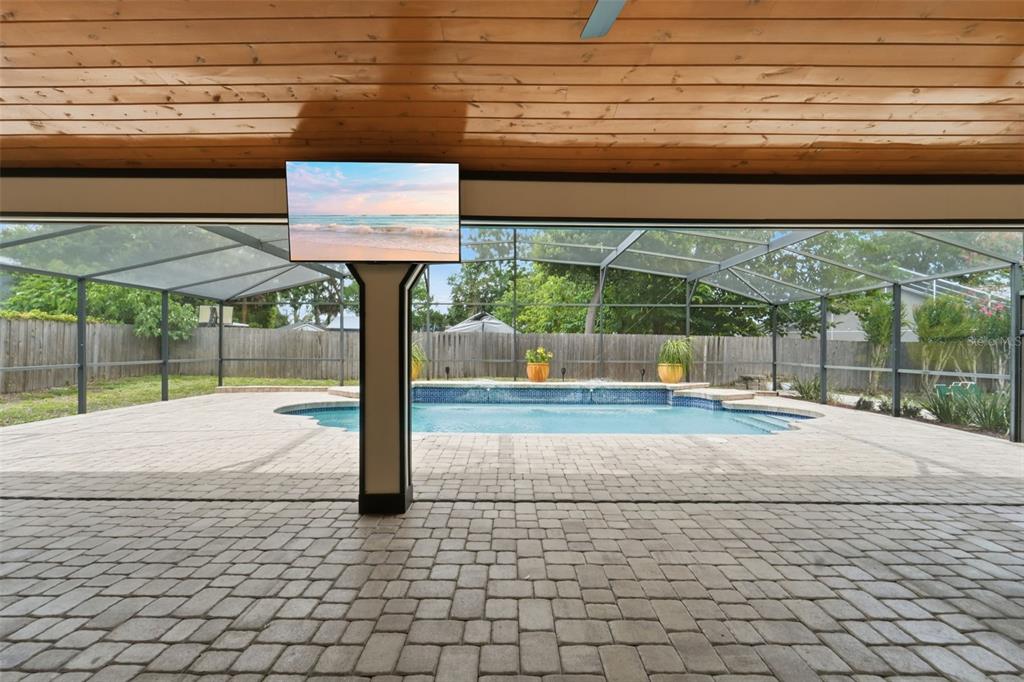 A covered patio with a television overlooks a screened-in swimming pool and a fenced backyard — 2309 SWEETWATER COUNTRY CLUB PLACE DRIVE, APOPKA, FL