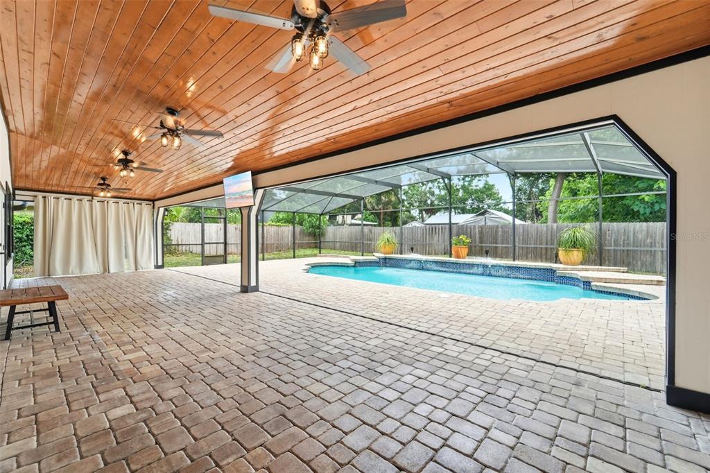 A covered patio with a wood-paneled ceiling overlooks a screened-in swimming pool and backyard — 2309 SWEETWATER COUNTRY CLUB PLACE DRIVE, APOPKA, FL