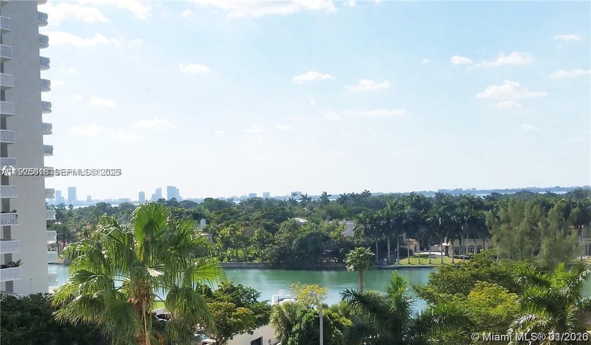 An elevated view shows a waterway, lush tropical landscaping, and distant city buildings — 5555 Collins Ave # 7T, Miami Beach FL 33140, MIAMI BEACH, FL