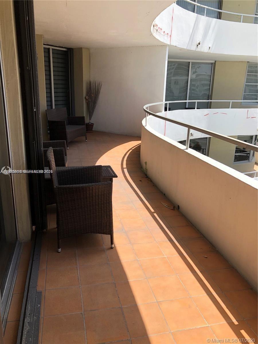 A curved balcony features tiled flooring, wicker furniture, and a white metal railing — 5555 Collins Ave # 7T, Miami Beach FL 33140, MIAMI BEACH, FL