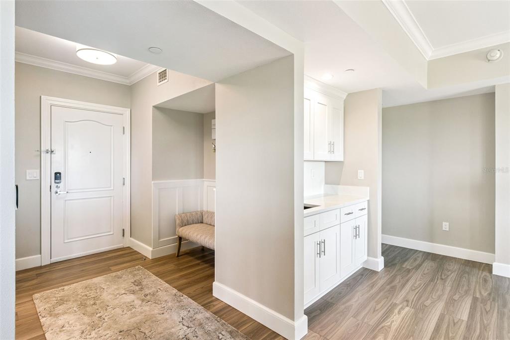 An entryway with wood-look flooring, a white door, a built-in bench, and a small kitchenette — 7593 GATHERING DRIVE UNIT 503, REUNION, FL