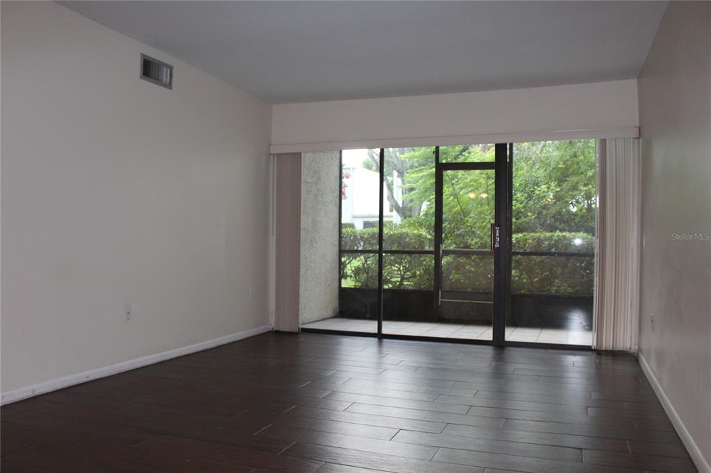 An empty room with dark wood-look flooring and a sliding glass door to a patio — 3294 S SEMORAN BOULEVARD UNIT 15, ORLANDO, FL