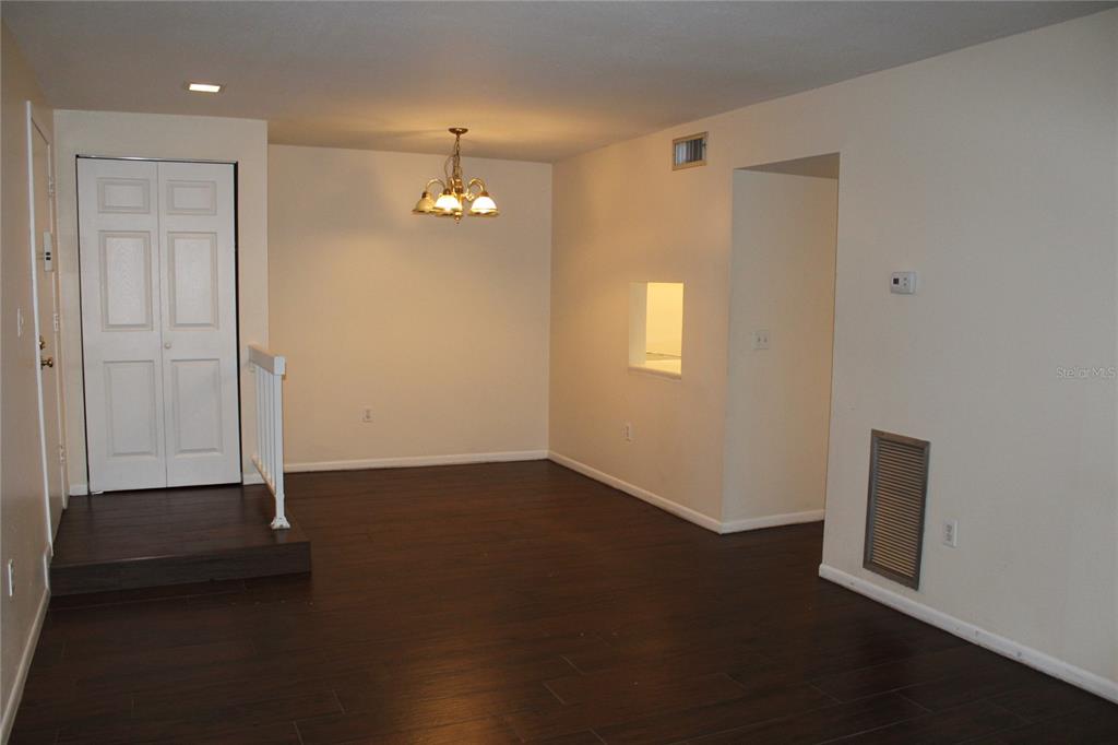 An empty dining area features dark wood-look flooring, a chandelier, and a white entry door — 3294 S SEMORAN BOULEVARD UNIT 15, ORLANDO, FL
