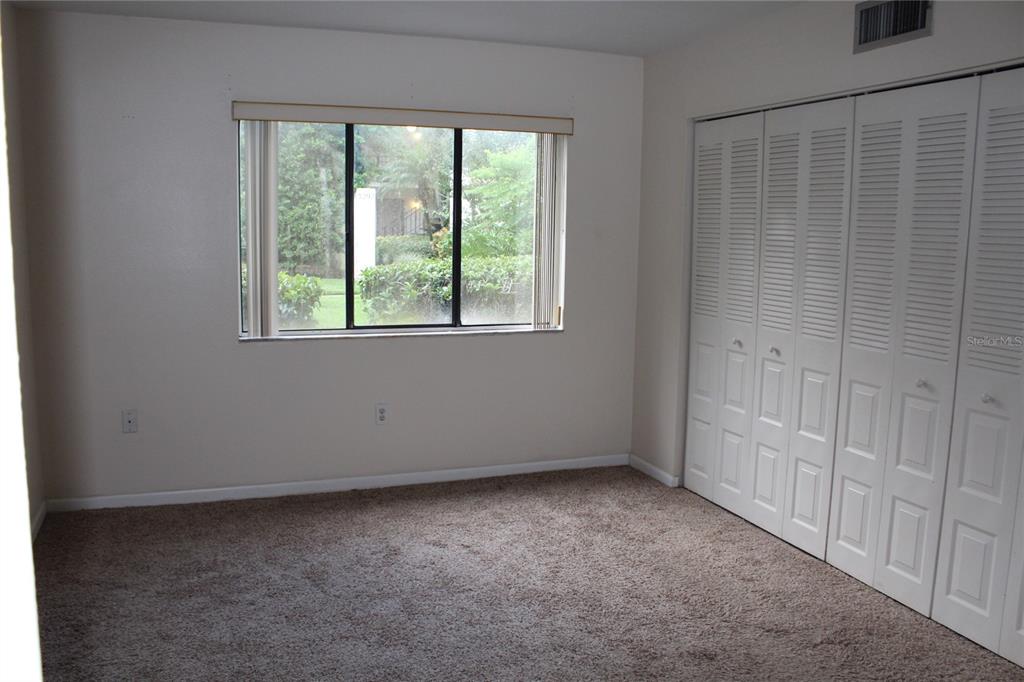 A bedroom with beige walls, brown carpet, a window, and white louvered closet doors — 3294 S SEMORAN BOULEVARD UNIT 15, ORLANDO, FL