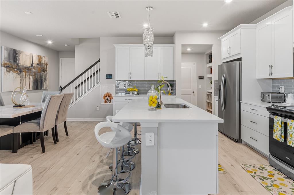 A modern kitchen features white cabinetry, a central island with bar stools, and light flooring — 4062 CLOUD HOPPER WAY, LUTZ, FL