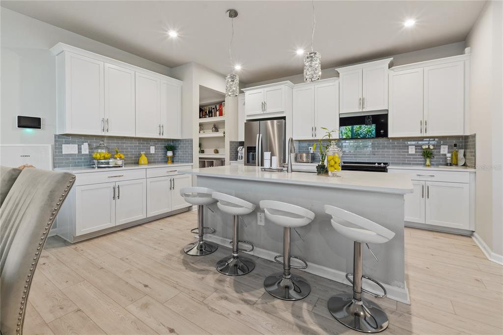 A modern kitchen features white cabinets, a gray tiled backsplash, and a central island with stools — 4062 CLOUD HOPPER WAY, LUTZ, FL