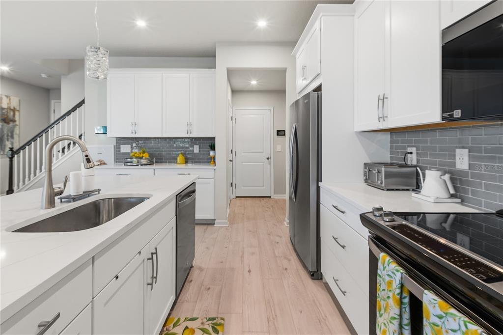 A modern kitchen features white cabinetry, a large island with a sink, and gray tile backsplash — 4062 CLOUD HOPPER WAY, LUTZ, FL