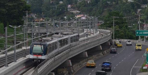 A train travels on an elevated track above a multi-lane road with surrounding hillside housing — Lot E-7a Calle Del Cerro Con La Calle Diagonal, Las Cumbres, FL