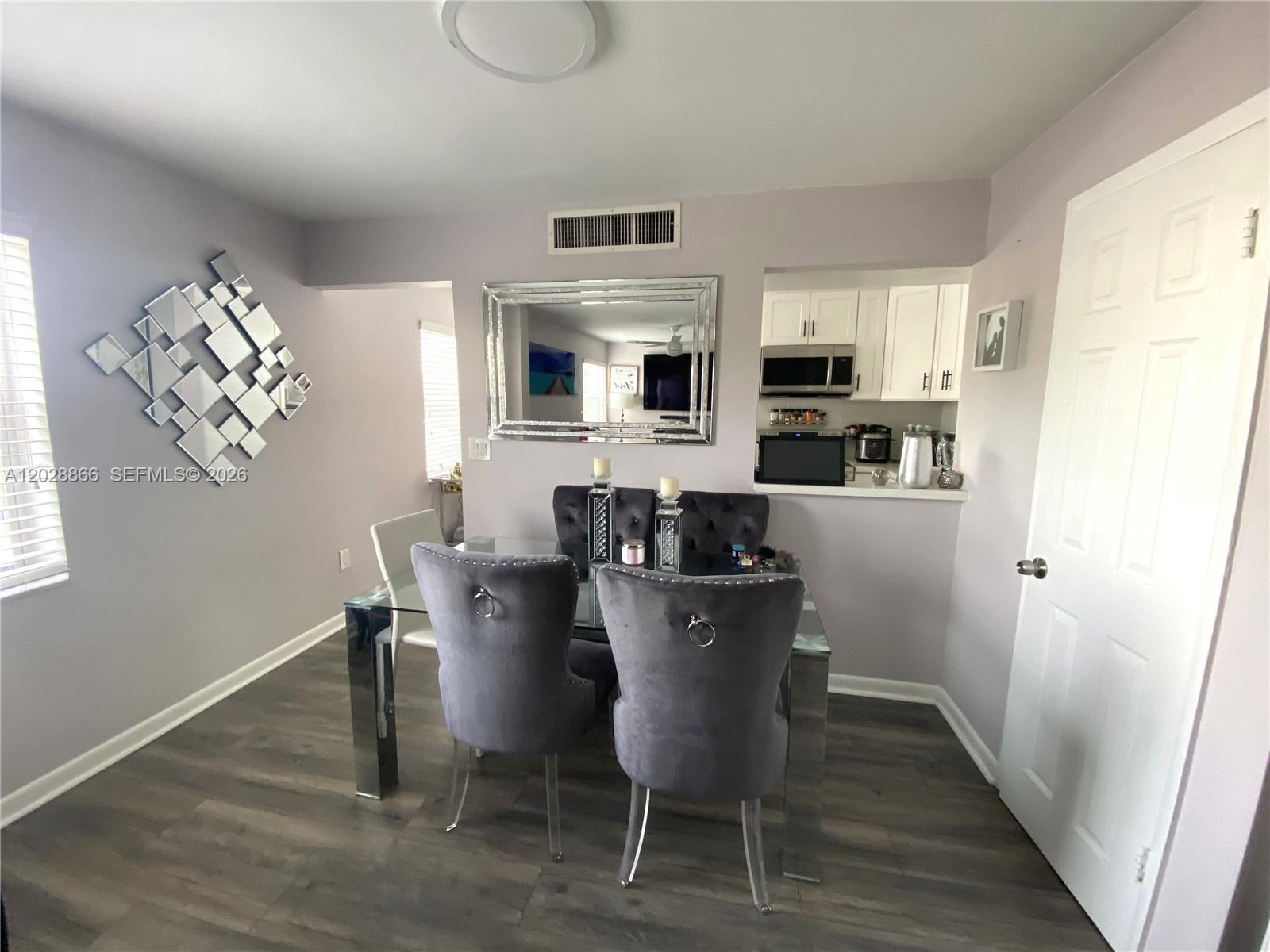 A dining room features a glass table, grey tufted chairs, and a large wall mirror — 1570 W 46th St # 214, Hialeah FL 33012, HIALEAH, FL