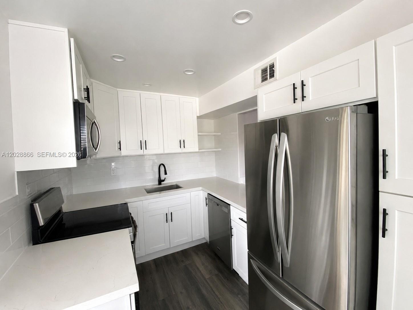 A modern kitchen features white cabinets, stainless steel appliances, and dark wood-look flooring — 1570 W 46th St # 214, Hialeah FL 33012, HIALEAH, FL