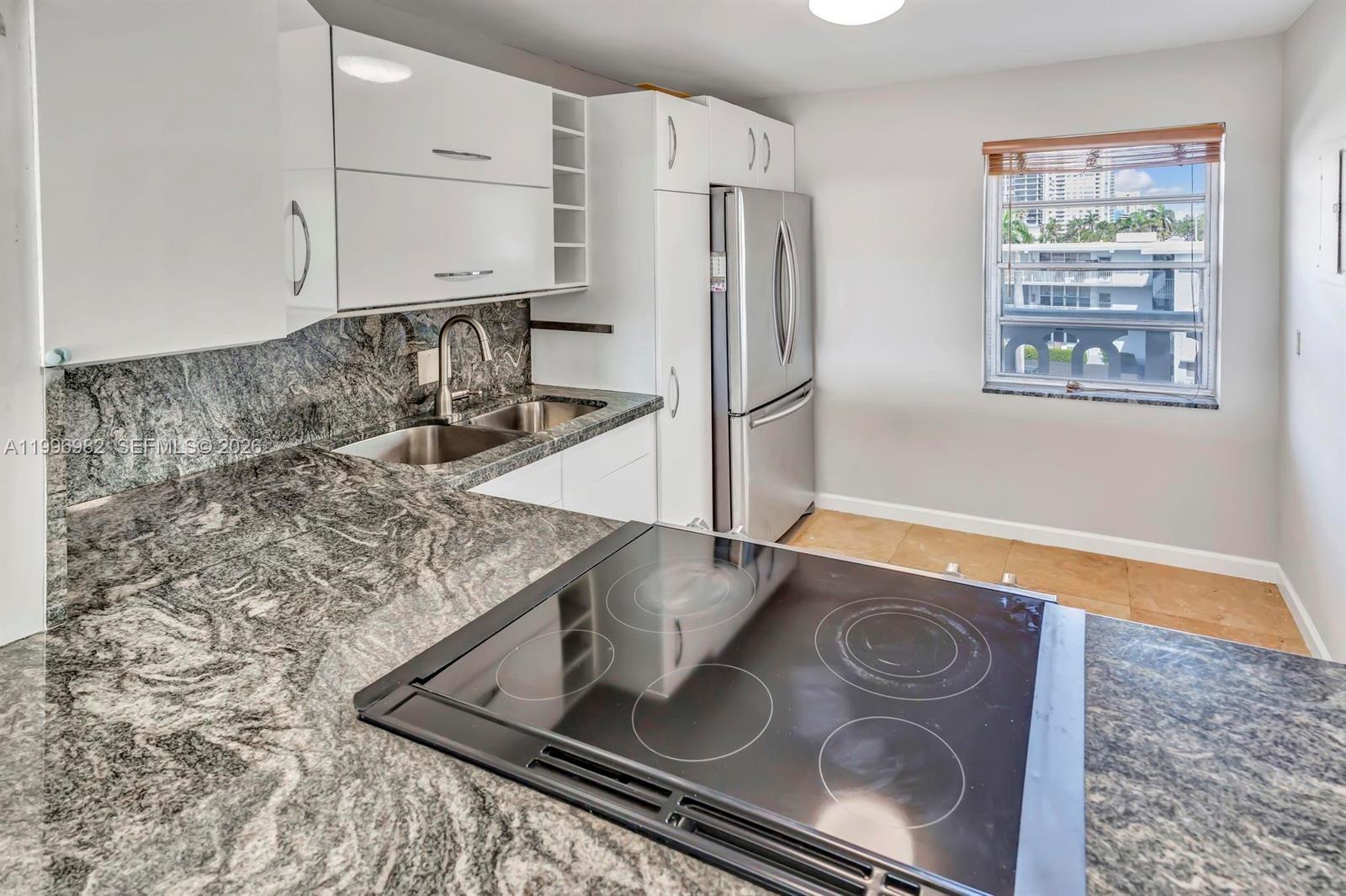 A kitchen features granite countertops, white cabinetry, stainless steel appliances, and a window view — 3199 S Ocean Dr # 406, Hallandale Beach FL 33009, HALLANDALE BEACH, FL