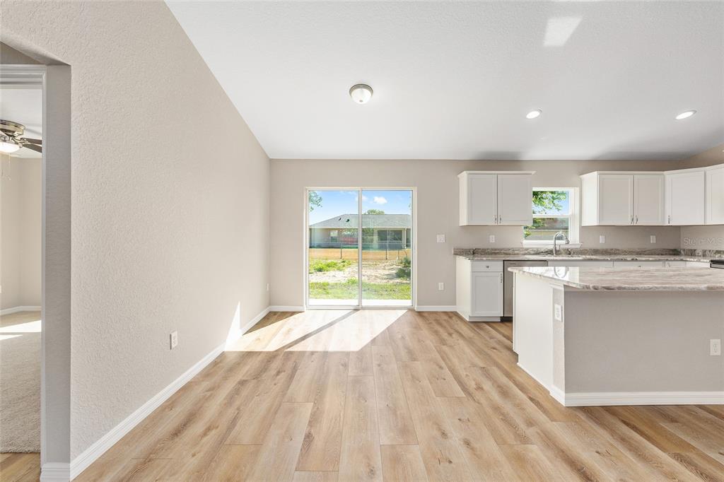 An open-concept kitchen and dining area features light wood-look flooring and a sliding glass door — 14664 SW 22ND PLACE, OCALA, FL