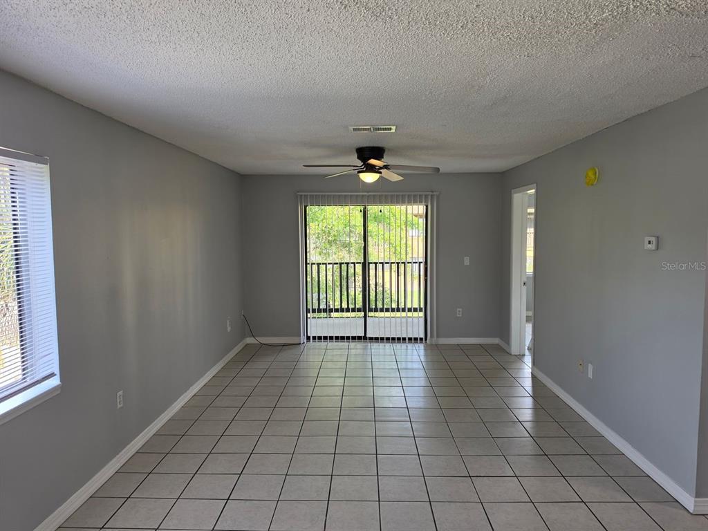 An empty living room features gray walls, tile flooring, a ceiling fan, and sliding glass doors — 2526 S OAK AVENUE UNIT A, SANFORD, FL