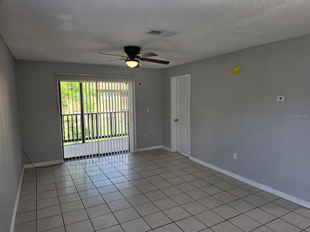 An empty room with gray walls, tile flooring, a ceiling fan, and a sliding glass door — 2526 S OAK AVENUE UNIT A, SANFORD, FL