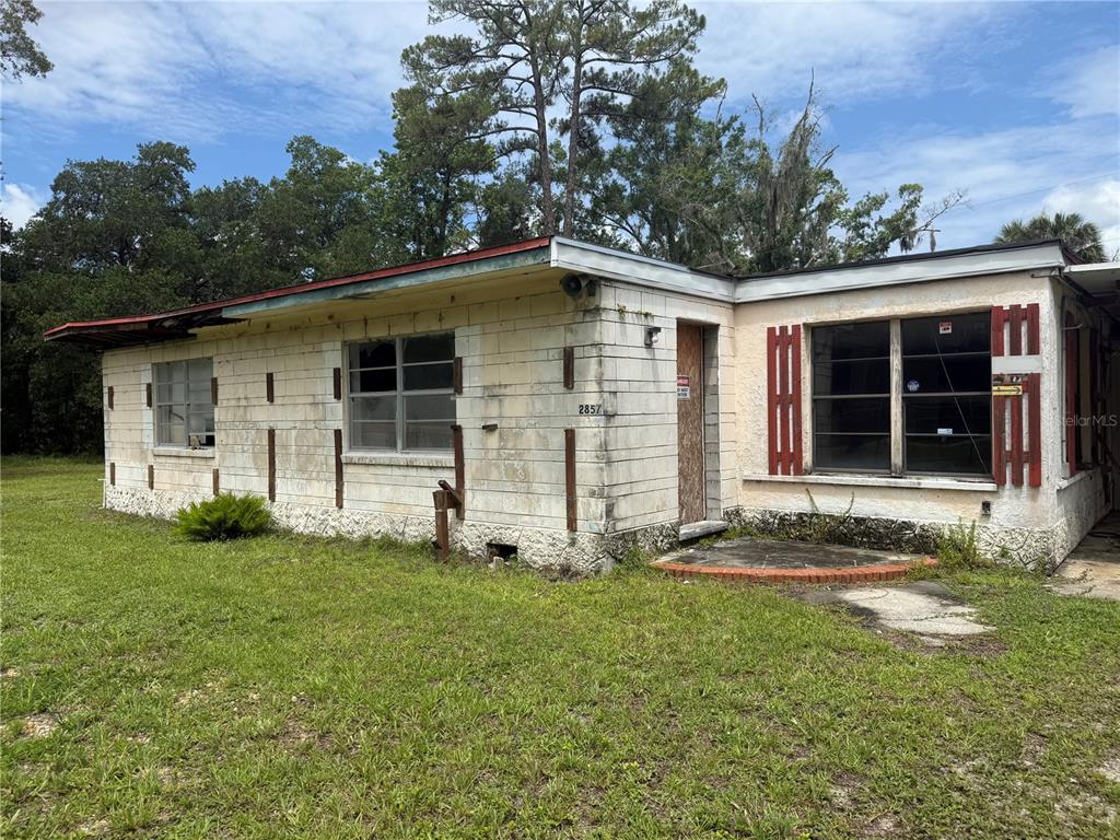 A single-story house with concrete block walls, boarded-up windows, and a red-trimmed roof — 2857 W NEW YORK AVENUE, DELAND, FL