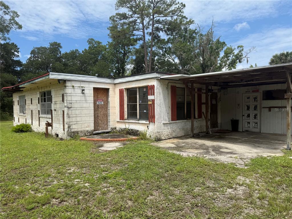 A single-story concrete block house with a carport and a boarded-up front door — 2857 W NEW YORK AVENUE, DELAND, FL
