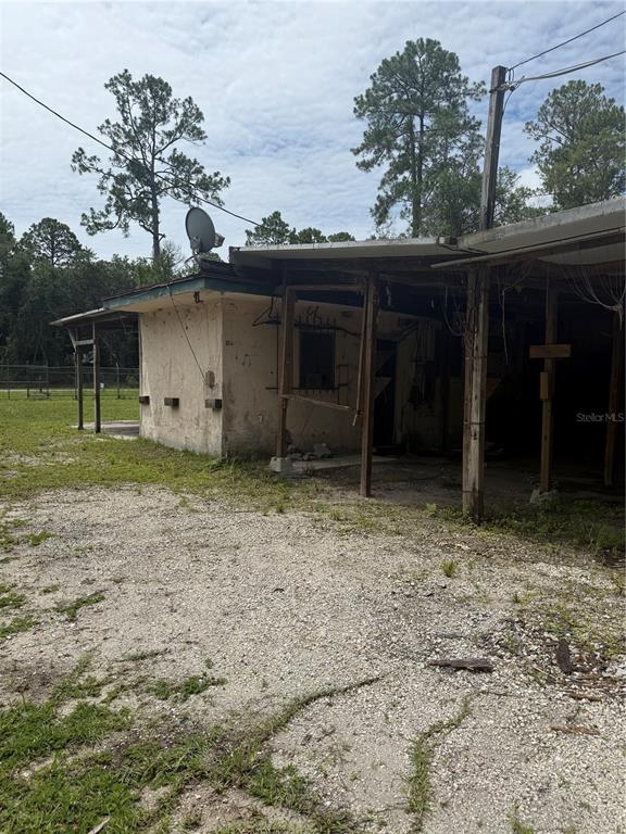 An exterior view of a weathered, single-story building with a covered porch and gravel yard — 2857 W NEW YORK AVENUE, DELAND, FL