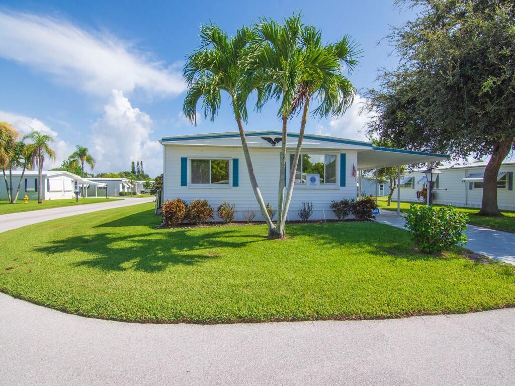 A white mobile home with blue shutters sits on a lawn with palm trees — 264 NE Cameo Way, Jensen Beach FL 34957, JENSEN BEACH, FL