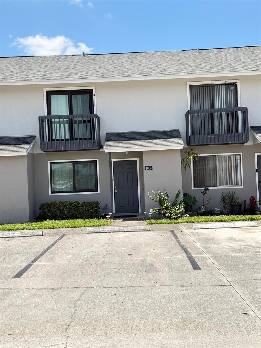 A two-story residential building exterior features a gray door, balconies, and a concrete parking area — 4803 Pier Drive, FL 33463, FL