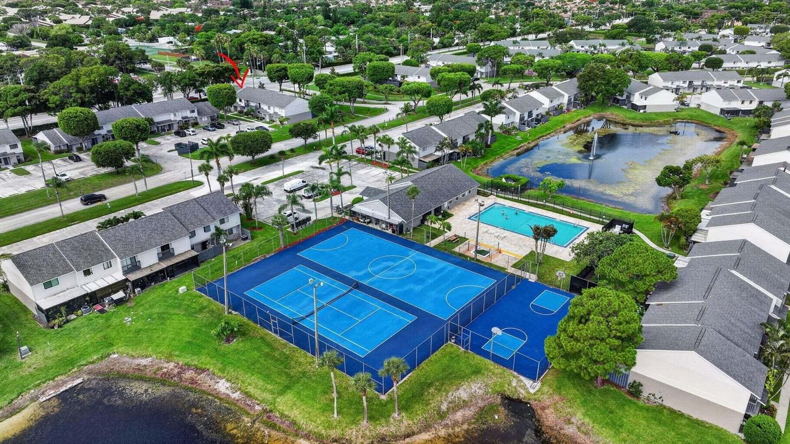 An aerial view of a residential complex featuring a swimming pool, tennis courts, and pond — 4803 Pier Drive, FL 33463, FL
