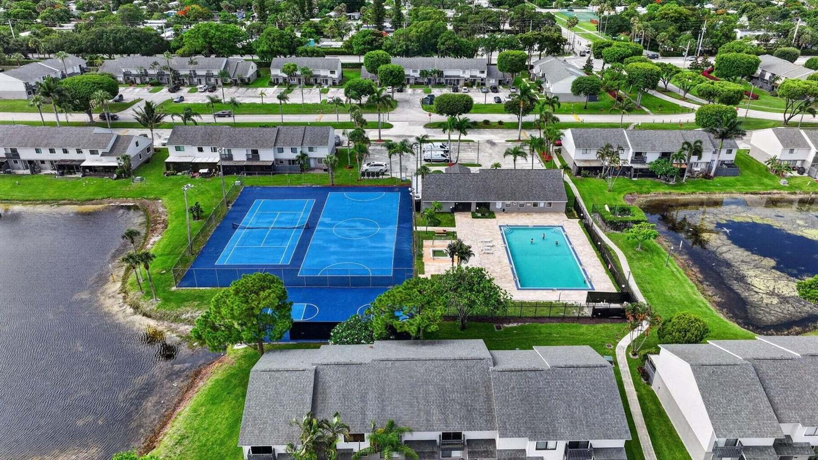 An aerial view of a residential community featuring a swimming pool and blue sports courts — 4803 Pier Drive, FL 33463, FL
