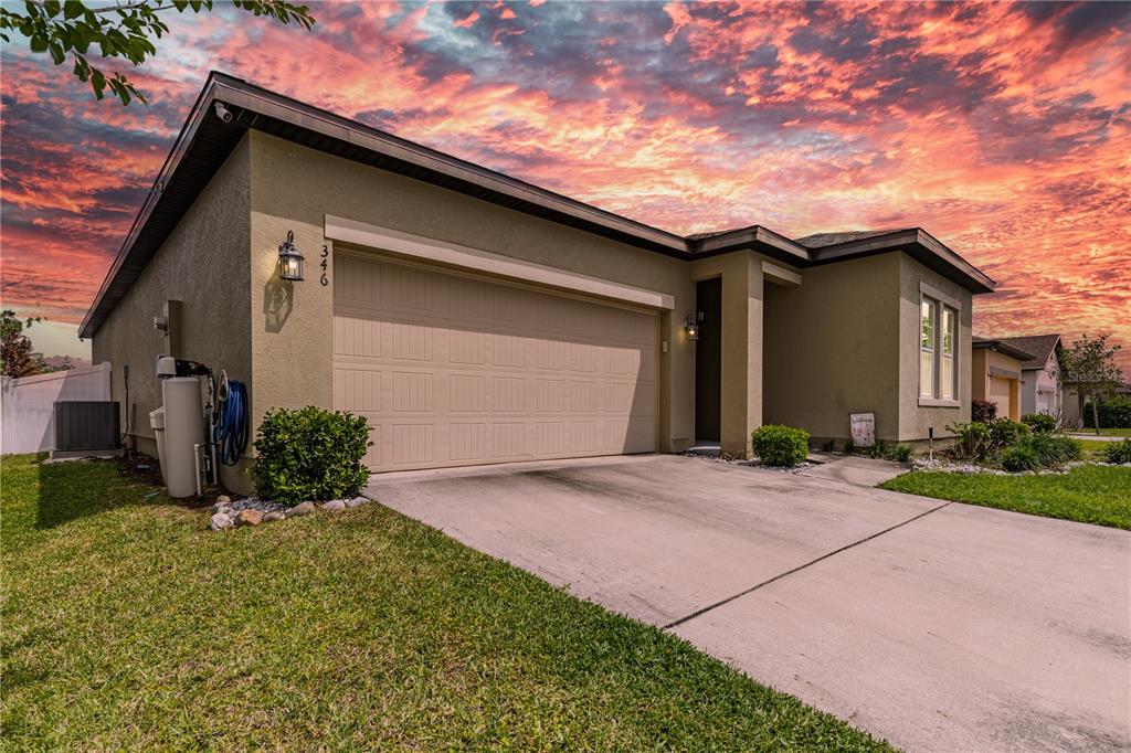 A tan single-story house with a two-car garage and a concrete driveway at sunset — 346 EAGLECREST DRIVE, HAINES CITY, FL