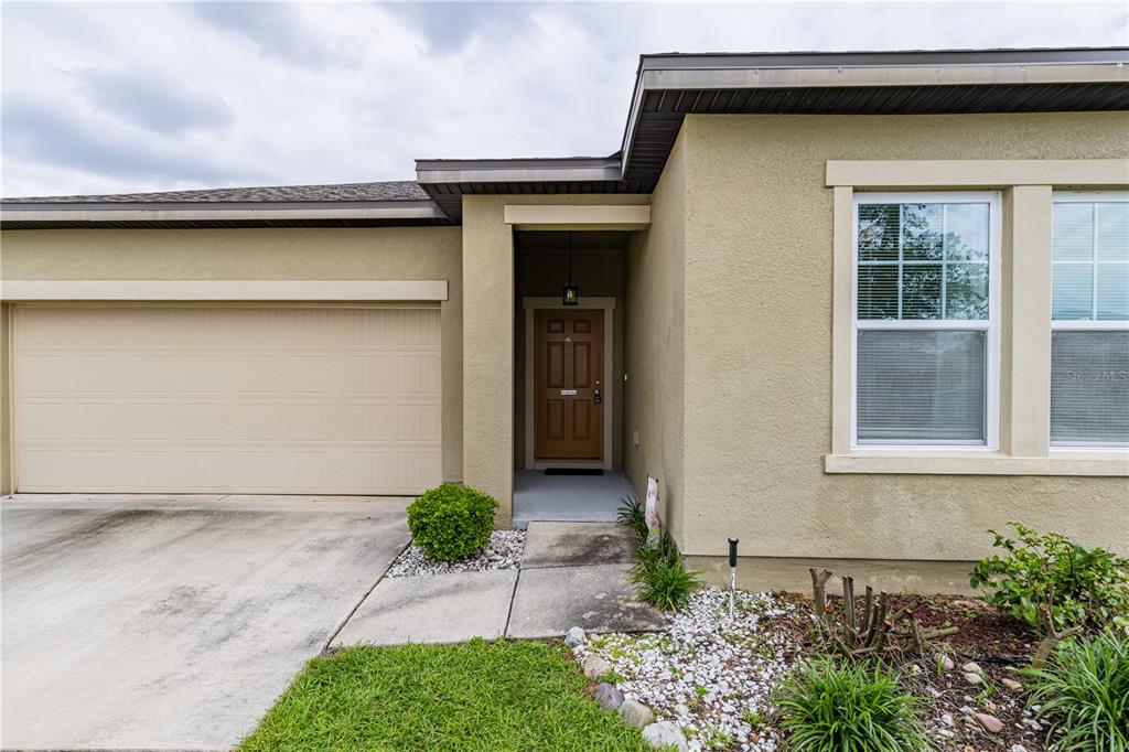 The exterior of a tan stucco house features a garage, a recessed entryway, and windows — 346 EAGLECREST DRIVE, HAINES CITY, FL