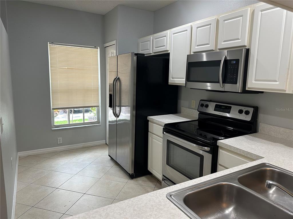 A kitchen features white cabinets, stainless steel appliances, a window with blinds, and tiled flooring — 8563 HUNTERS KEY CIRCLE, TAMPA, FL