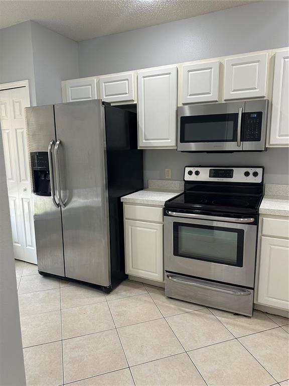 A kitchen features white cabinets, stainless steel appliances, and light-colored tile flooring — 8563 HUNTERS KEY CIRCLE, TAMPA, FL